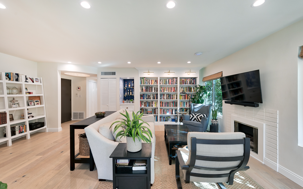 Modern ADU living room interior with built-in bookshelves, recessed lighting, fireplace, wall-mounted TV, and open seating area.