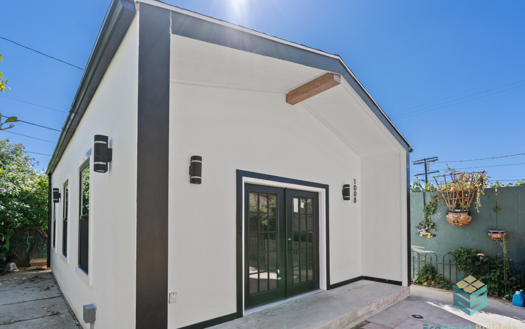Detached backyard ADU with modern white exterior, black trim, covered entry porch, and glass French doors.