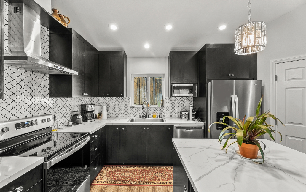 Modern ADU kitchen with black cabinets, white countertops, stainless steel appliances, patterned tile backsplash, and a center island.